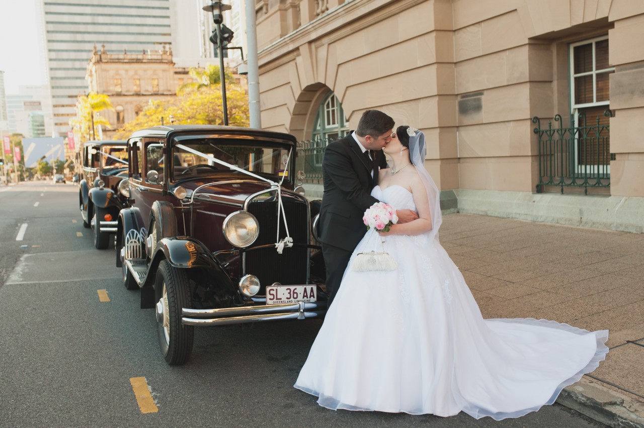Bride and Groom kissing next to their vintage wedding car