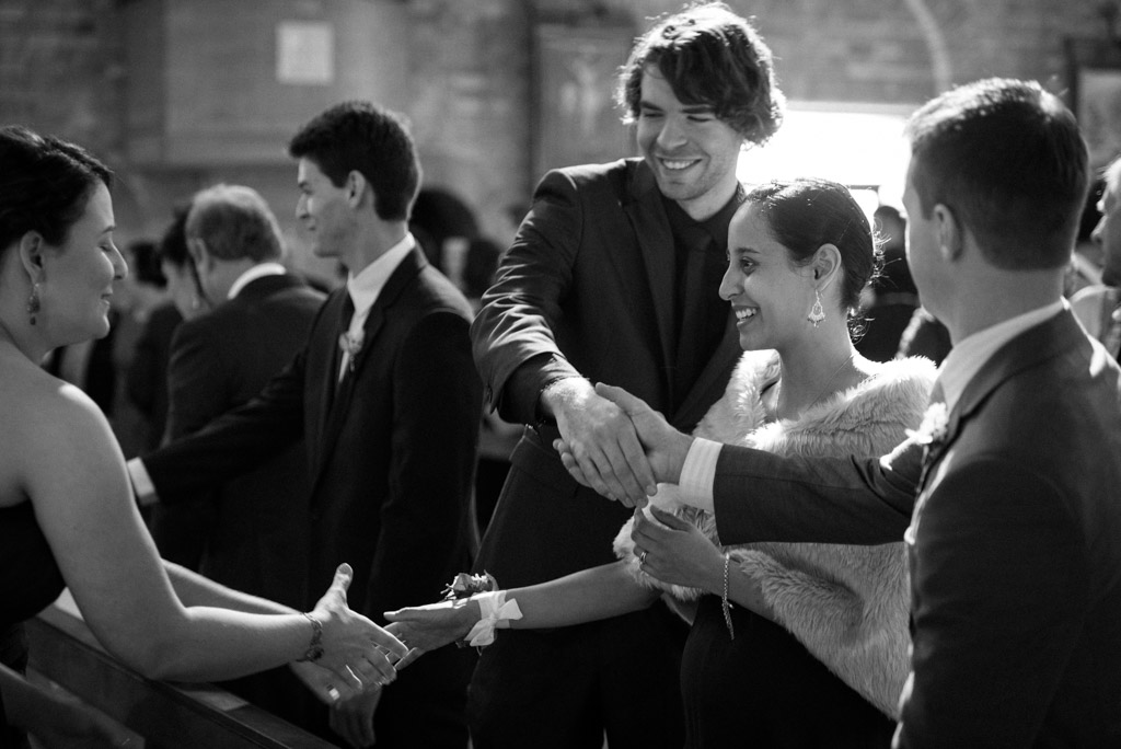 Black and white candid: wedding attendees greeting each other during the ceremony