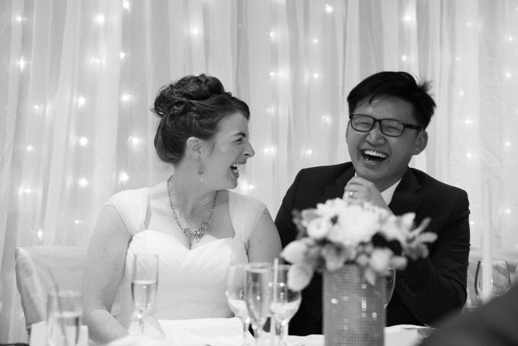Black and white candid: Shawn and Michaela laughing to the best man's speech