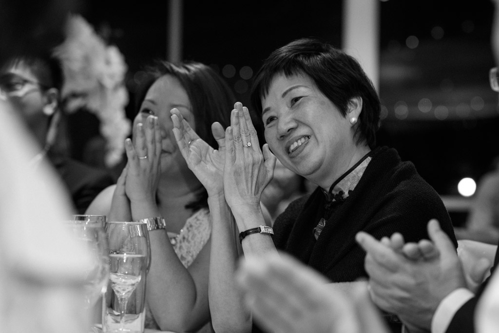 Black and white candid: Mother of the groom clapping to one of the speeches