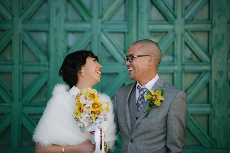 Bride and groom laughing against a teal door
