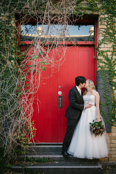 Bride and groom kissing against a red door at the London Woolstore, Teneriffe Wedding