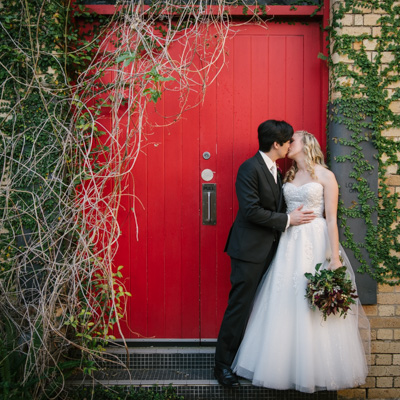 Bride and groom kissing against a red door with red vines in Teneriffe